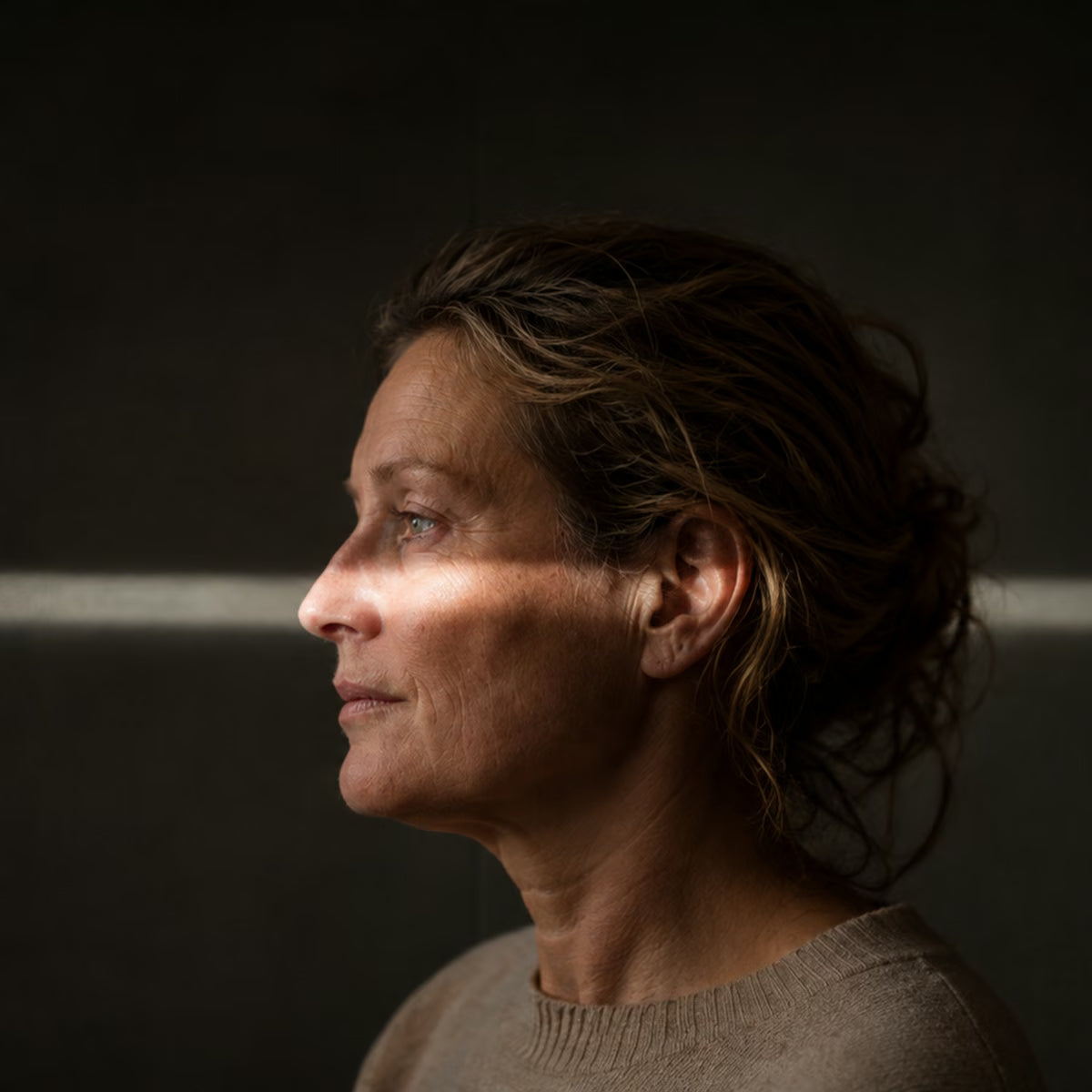 Ein Gesicht im Profil vor dunkler Wand, eine Linie aus Licht läuft über die Augen